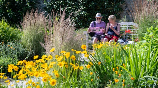 Visitors enjoy a peaceful moment whilst sat on a wooden bench at Bodnant Garden